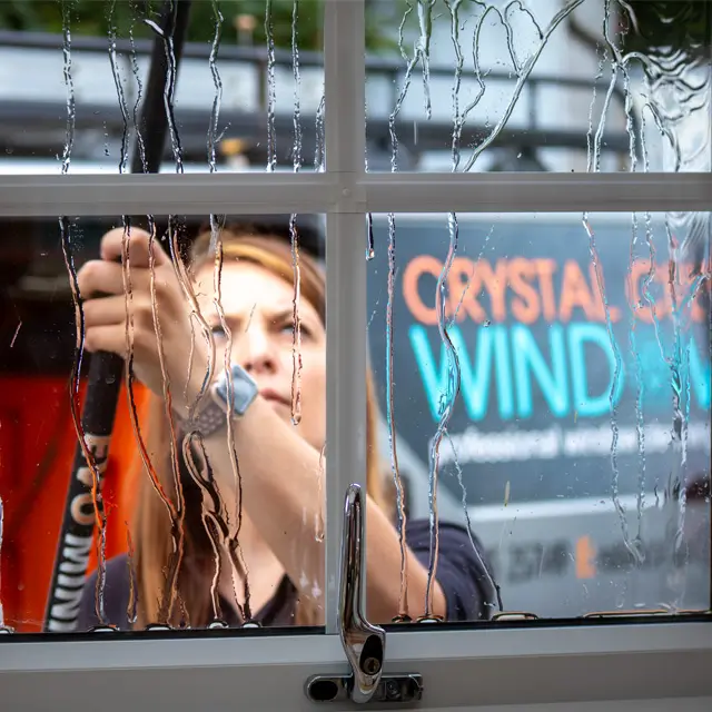 A professional cleaner from Crystal Clean Windows provides expert residential window cleaning, ensuring a streak-free finish for a local home.